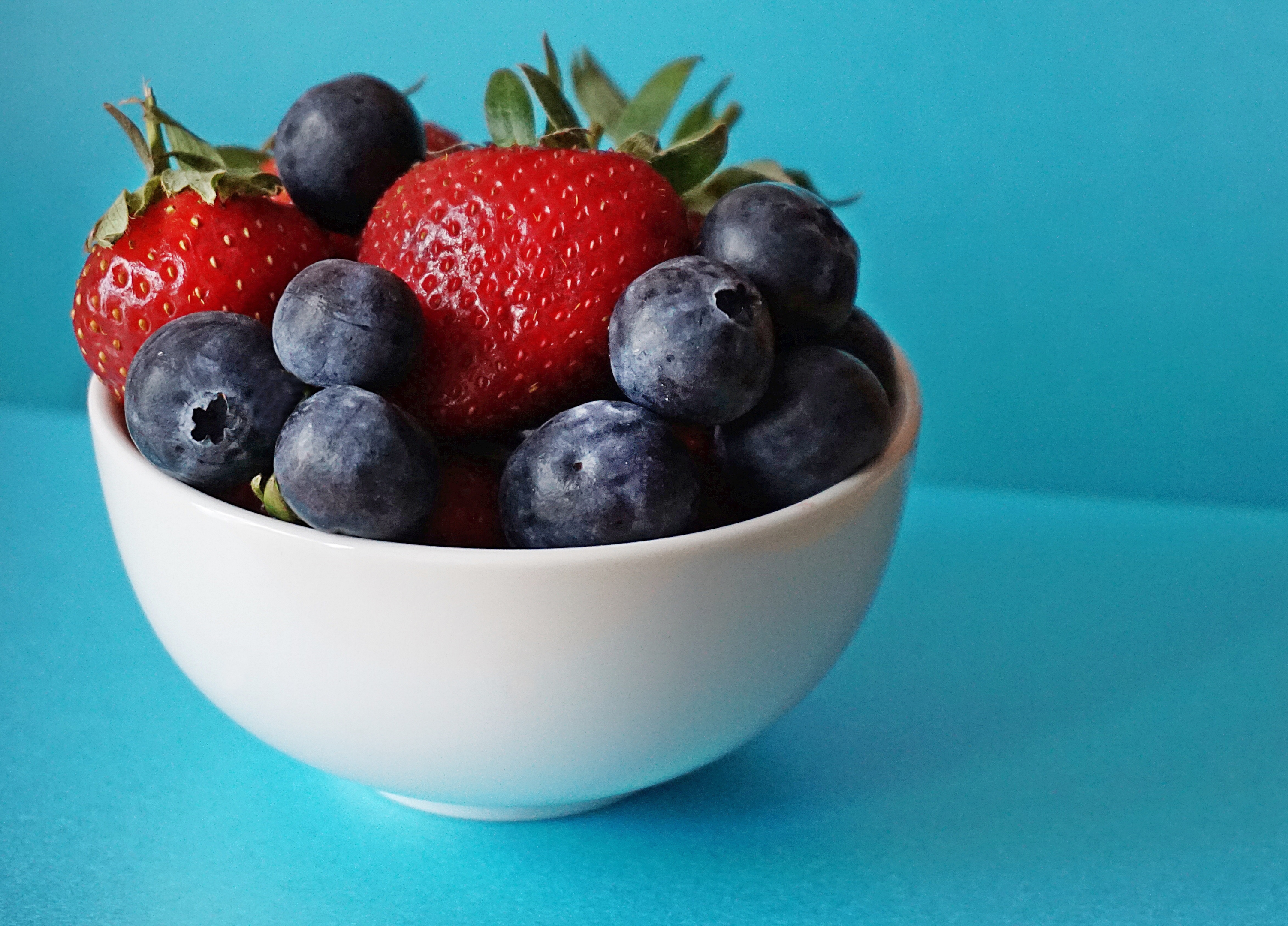 Fresh blueberries and strawberries in a white bowl, vibrant and healthy fruits that aid in combating constipation and supporting digestive well-being